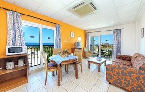 A bright living room with a balcony, a dining table, and a sofa. - Atlantica Aqua Blue (Paralimni)