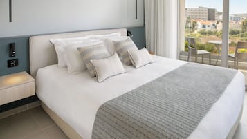 A neatly made bed with a patterned throw, a bedside table with a lamp, and a view of the city through large windows.
