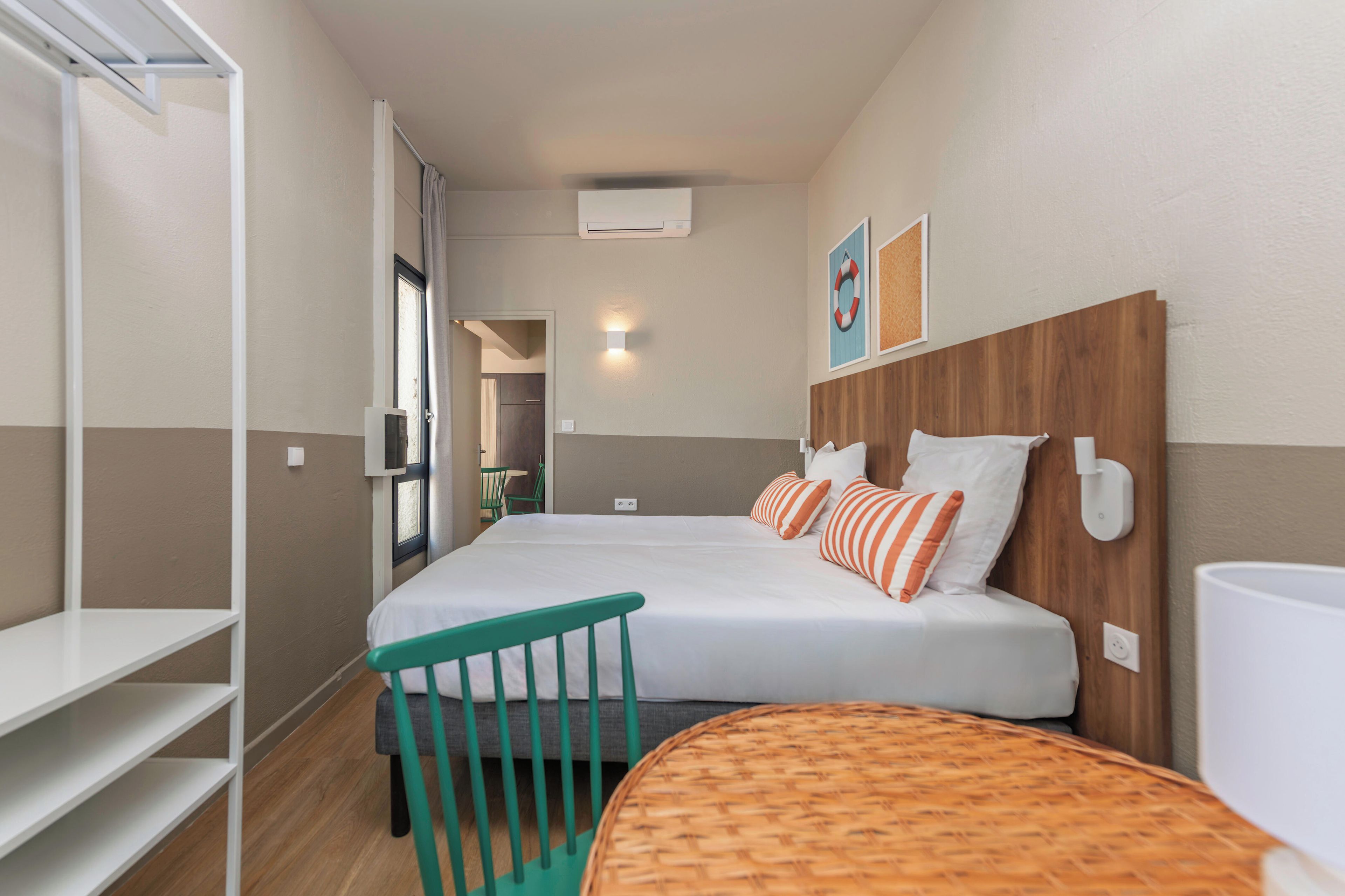 A hotel room with a bed, a chair, a small table, and a wall-mounted light fixture.