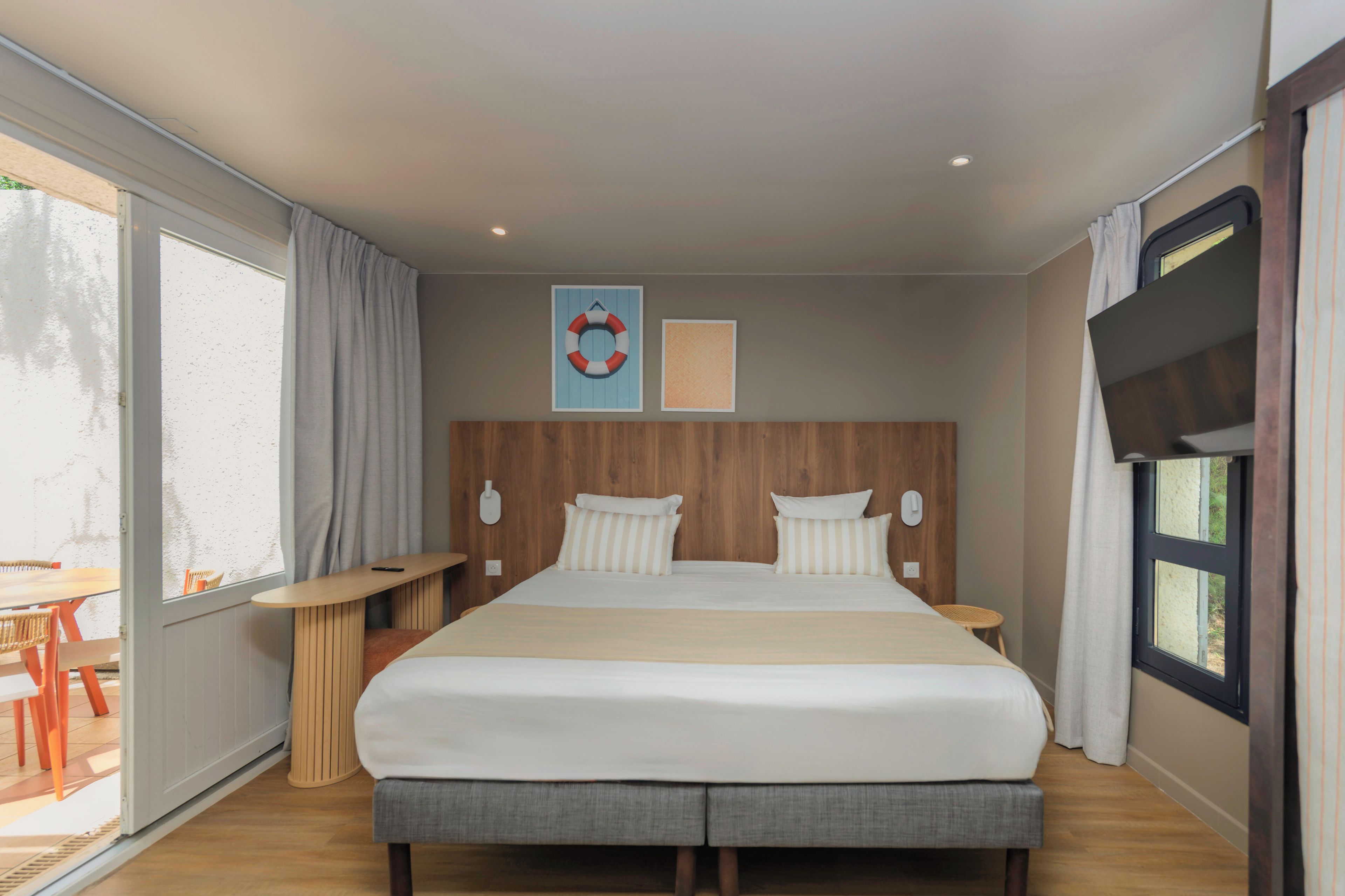 A modern hotel room with a large bed, a wooden headboard, a flat-screen TV, and a large window with curtains.