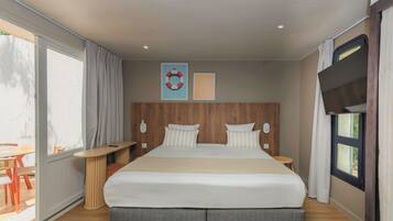 A modern hotel room with a large bed, a wooden headboard, a flat-screen TV, and a large window with curtains.