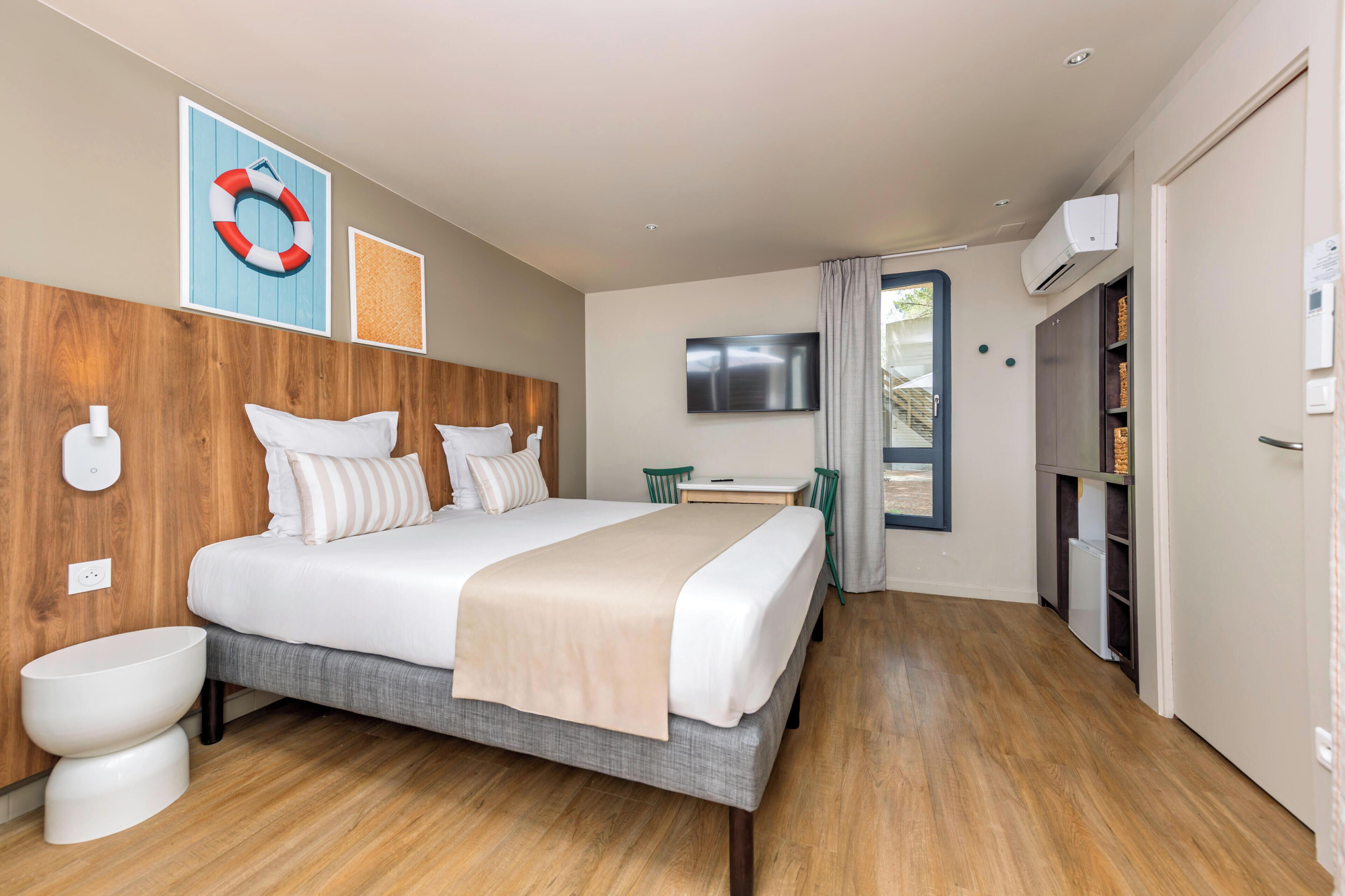 Une chambre d’hôtel moderne avec une tête de lit en bois, un grand lit, une table de chevet, un téléviseur et une armoire.