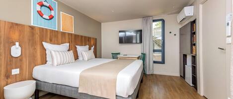 Une chambre d’hôtel moderne avec une tête de lit en bois, un grand lit, une table de chevet, un téléviseur et une armoire.