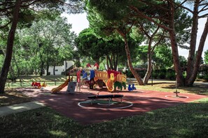 Un parque infantil con toboganes y estructuras para escalar, rodeado de árboles.