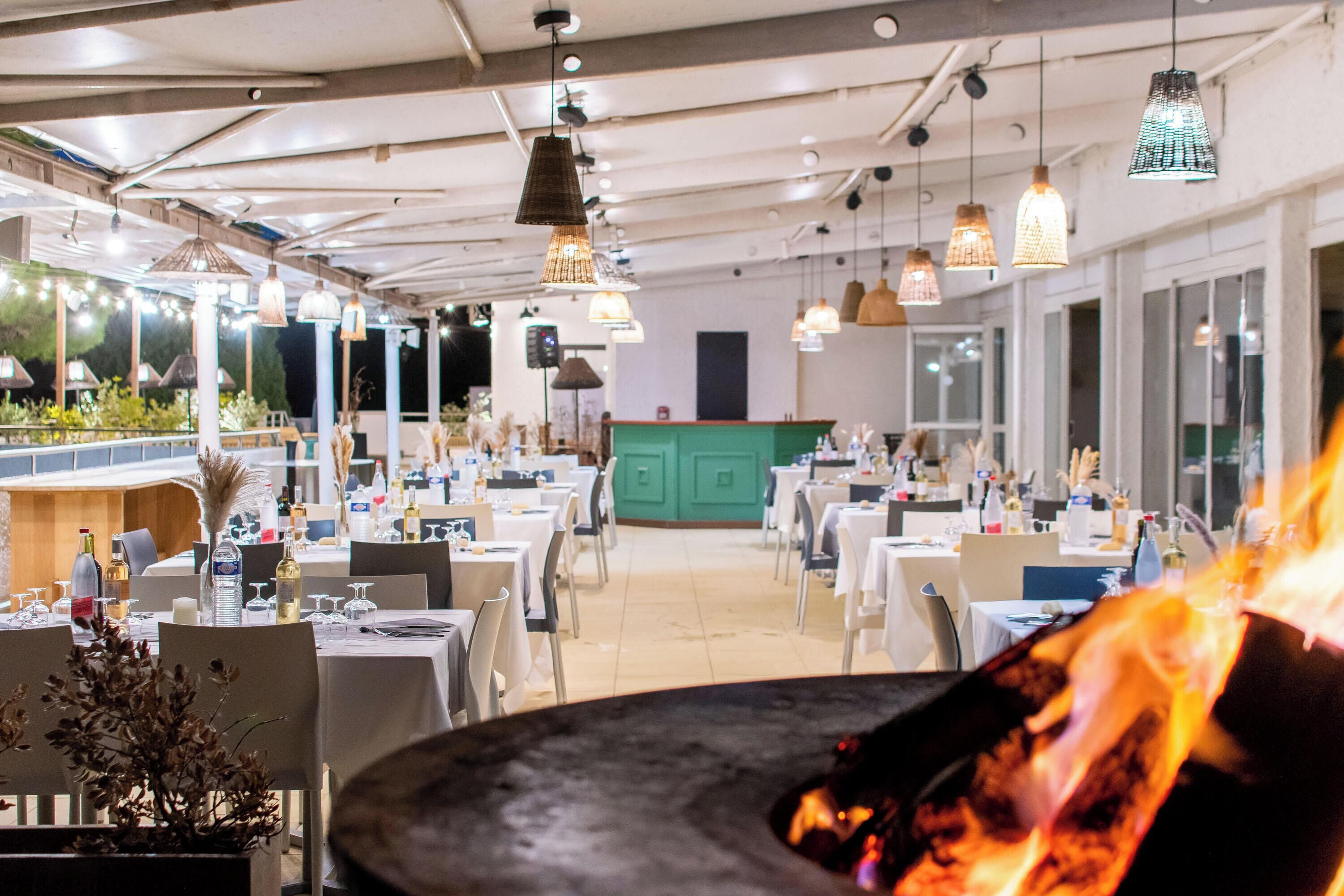 A restaurant with tables and chairs, a green counter, and hanging pendant lights.