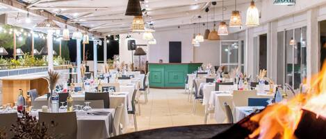 A restaurant with tables and chairs, a green counter, and hanging pendant lights.