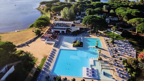 Eine Vogelperspektive zeigt ein Resort mit einem großen Schwimmbad, Liegestühlen und einem Strandabschnitt.