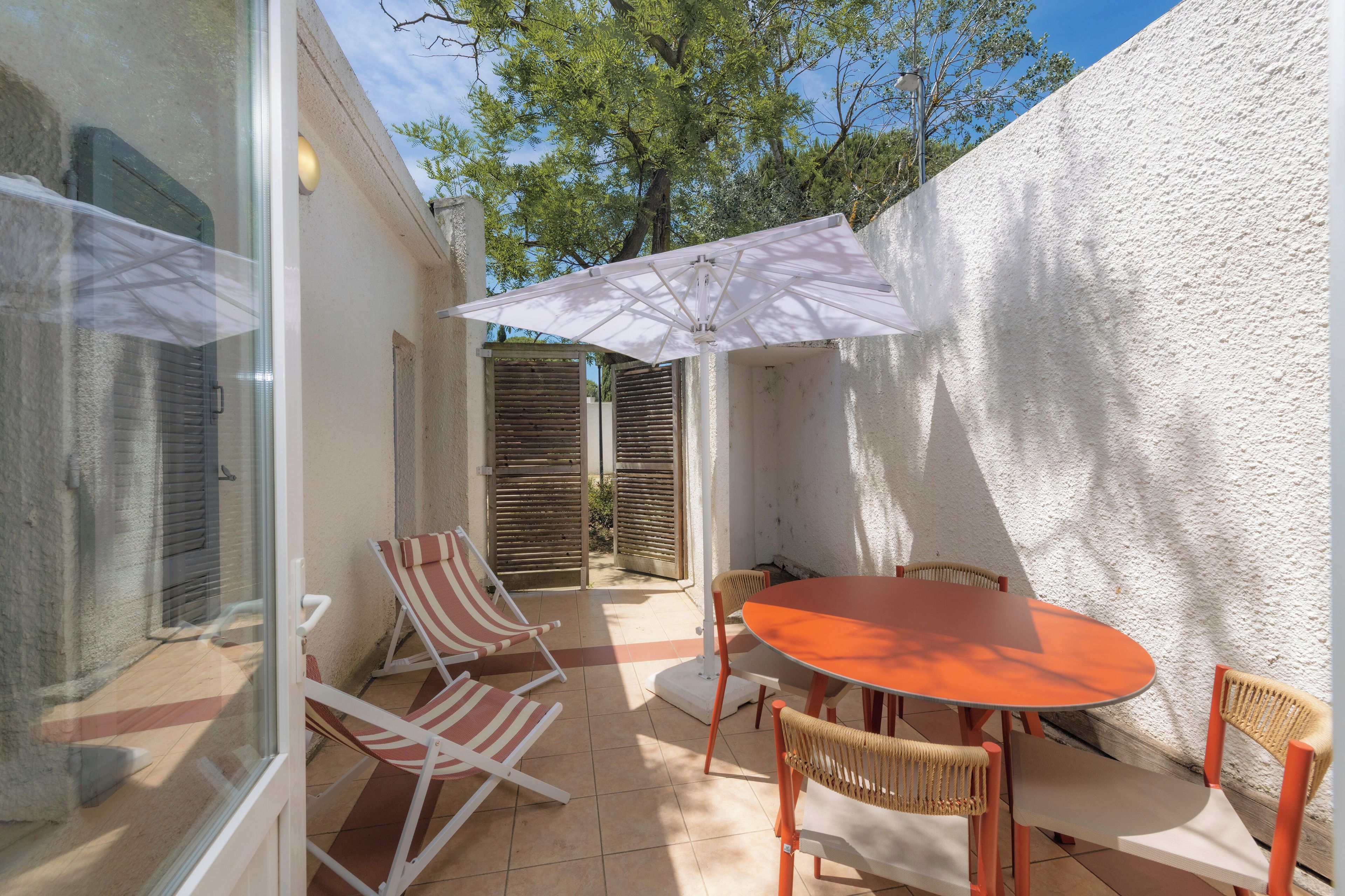Een terras met een tafel, stoelen, een glazen deur en een witte muur.