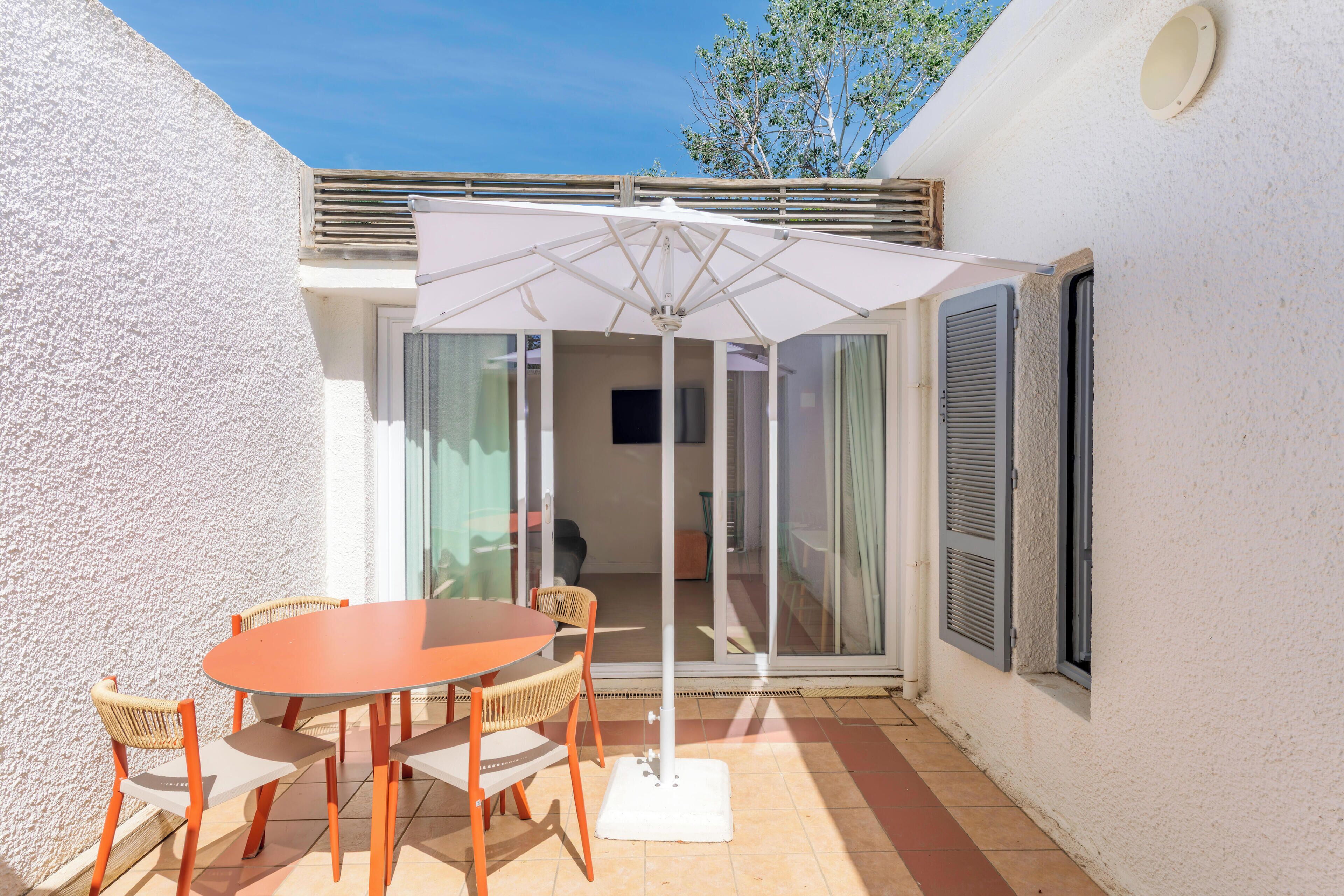 A patio with a table and chairs, a white umbrella, and a sliding glass door leading to an interior space.