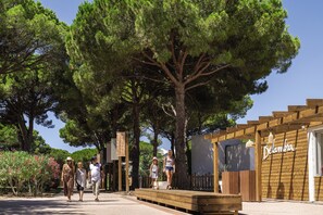 Eine Holzpergola mit einem Schild, auf dem 'Delambra' steht, in einem Garten mit Bäumen und einem Weg.