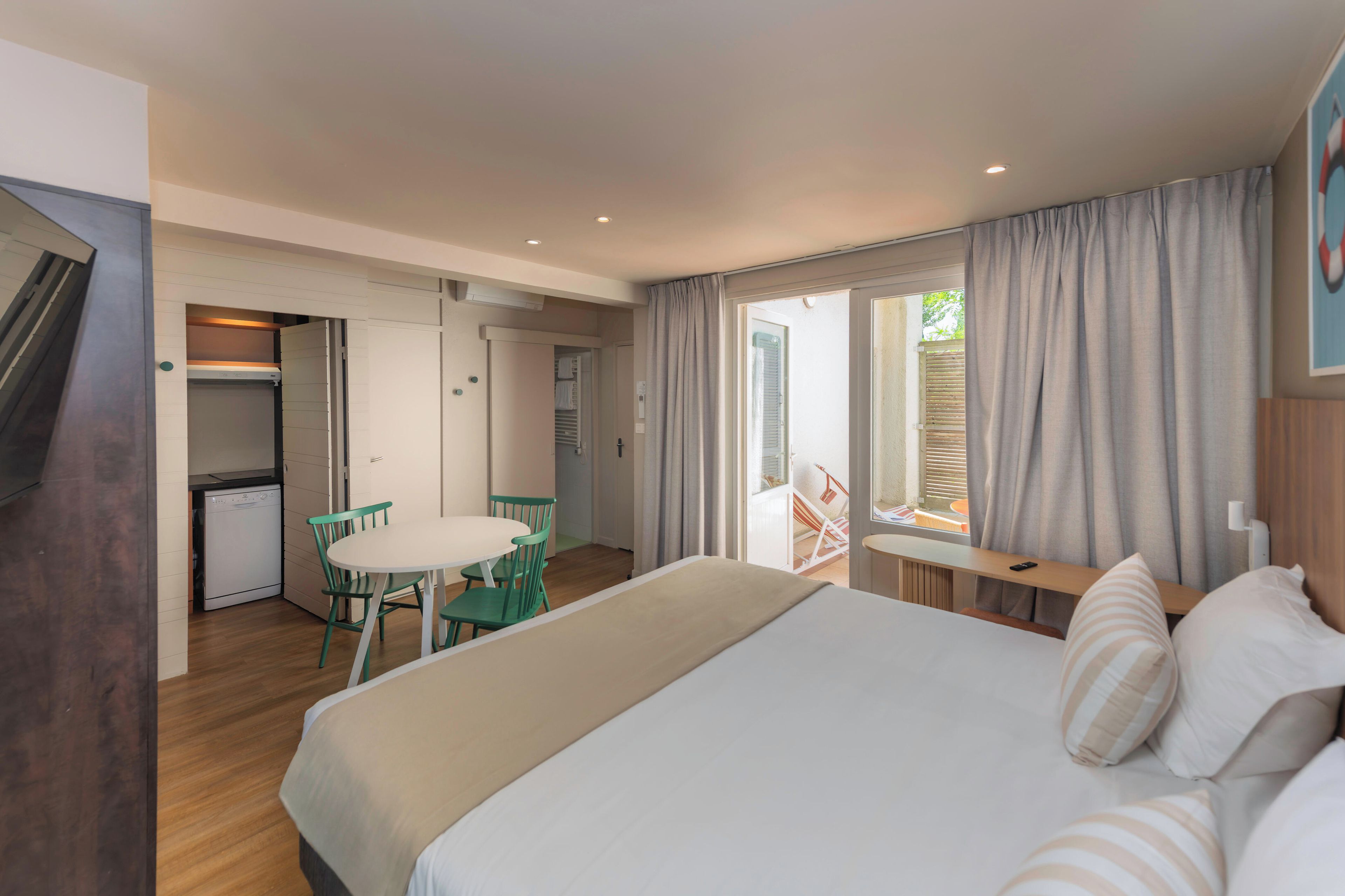 A hotel room with a bed, a dining table with chairs, a kitchenette, and a bathroom visible through an open door.