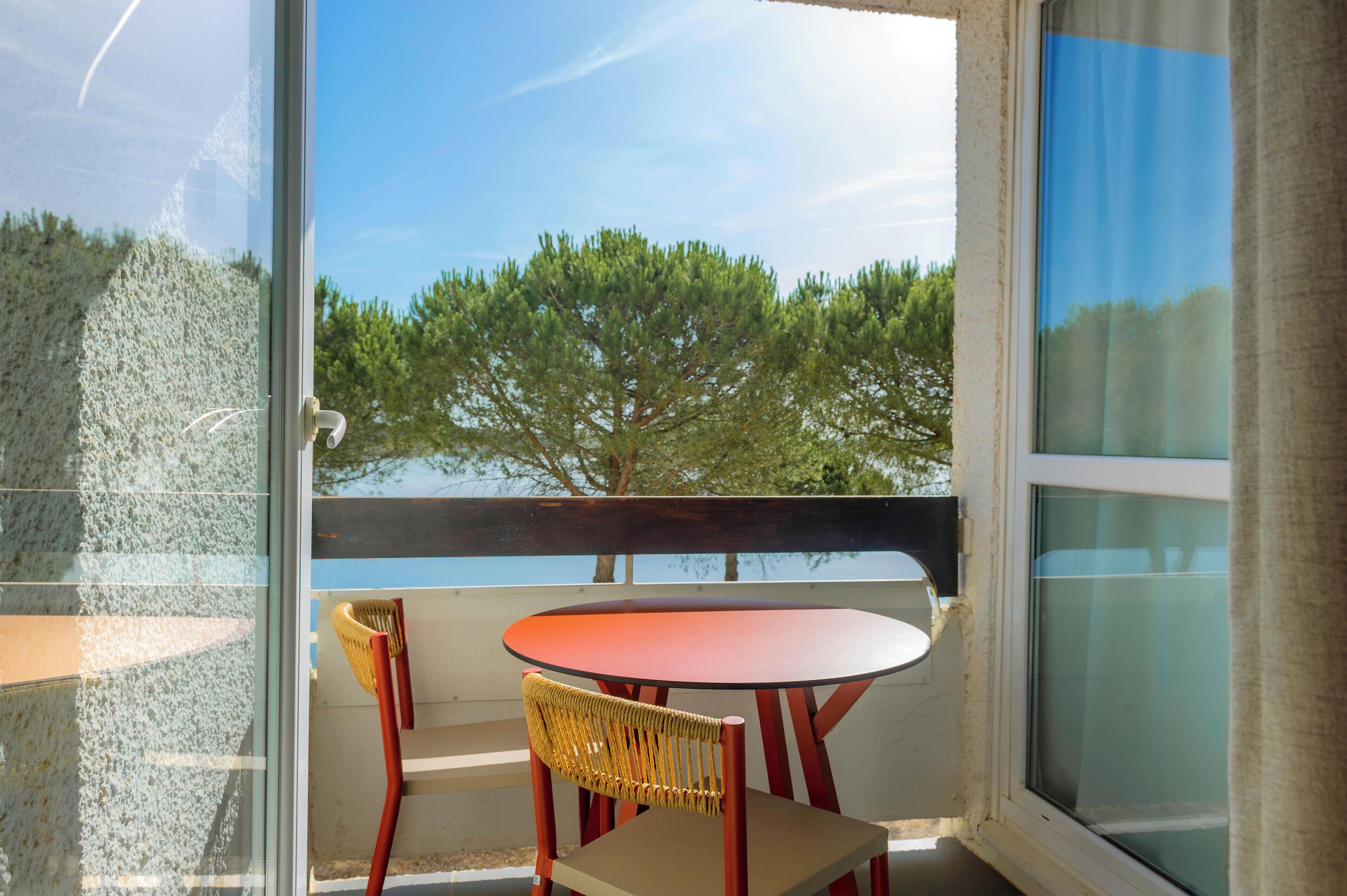 A balcony with a table and chairs, a view of trees, and a clear sky.