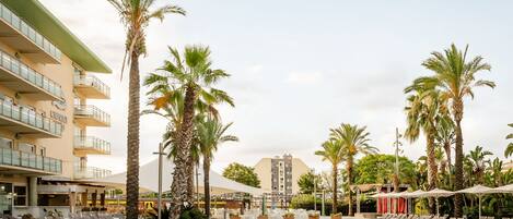 A hotel pool area with lounge chairs, palm trees, and a building with balconies.