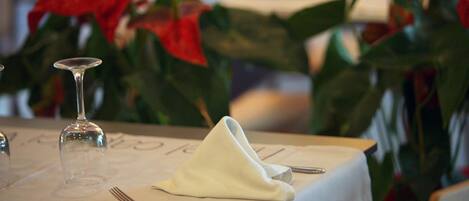 Una mesa dispuesta con servilleta blanca, un tenedor y una copa de vino, con flores rojas de fondo.