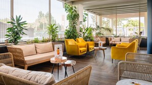 A modern lounge area with wicker furniture, large windows, and indoor plants.