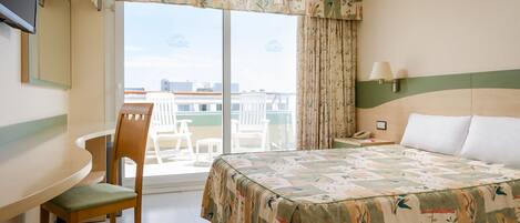 Habitación de hotel con cama, escritorio, silla, ventana con cortinas y vista a edificios.