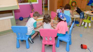 Children learn and play in a lively classroom with colorful chairs and tables.
