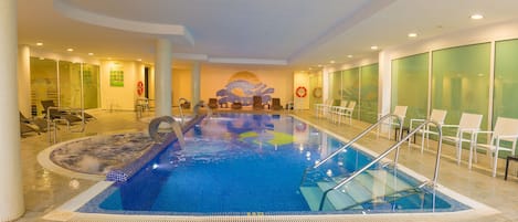 Una piscina interior con agua cristalina, un jacuzzi y sillones de descanso.