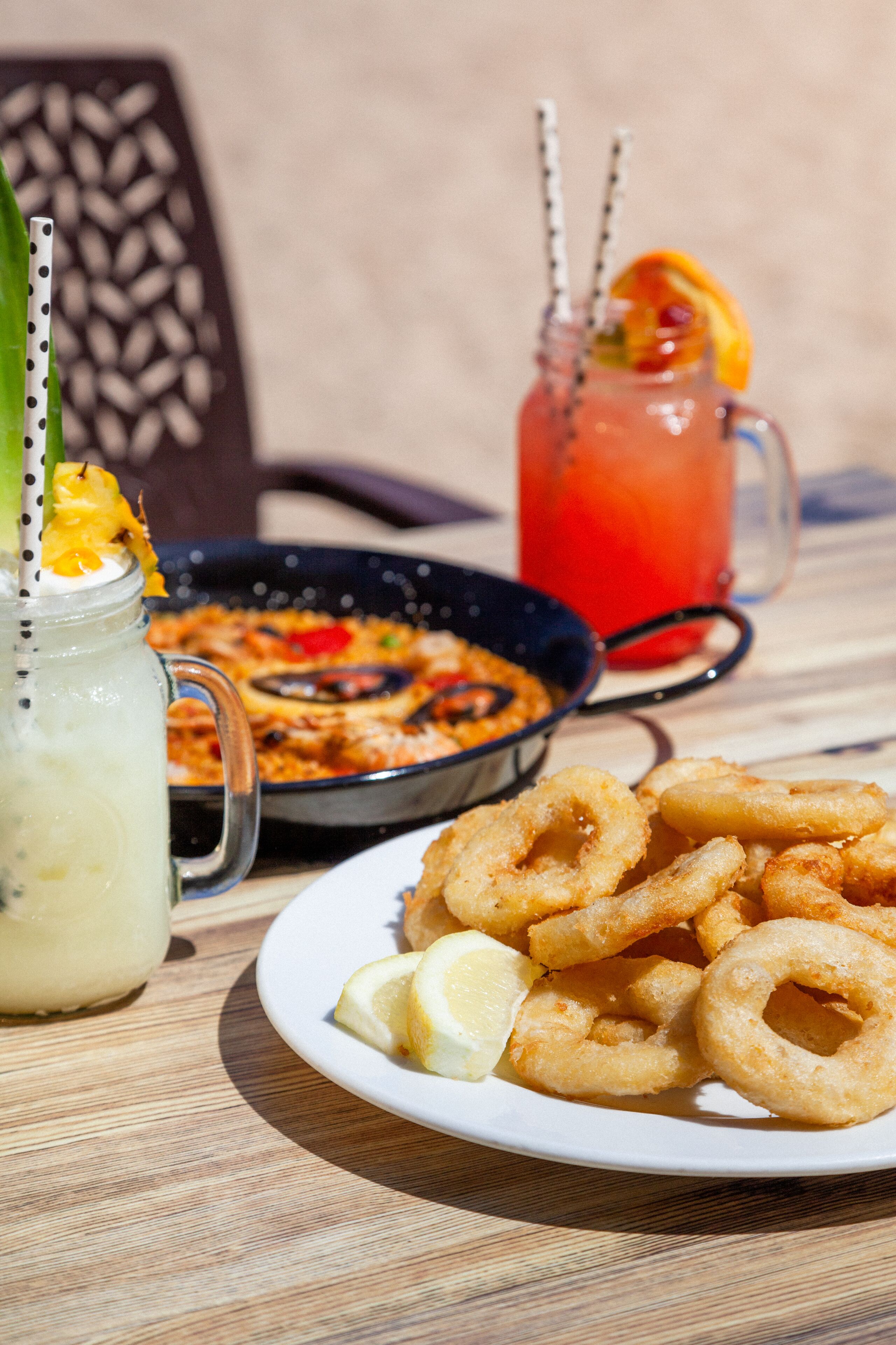 A table with a plate of fried calamari, a bowl of paella, and a pitcher of iced tea with straws.