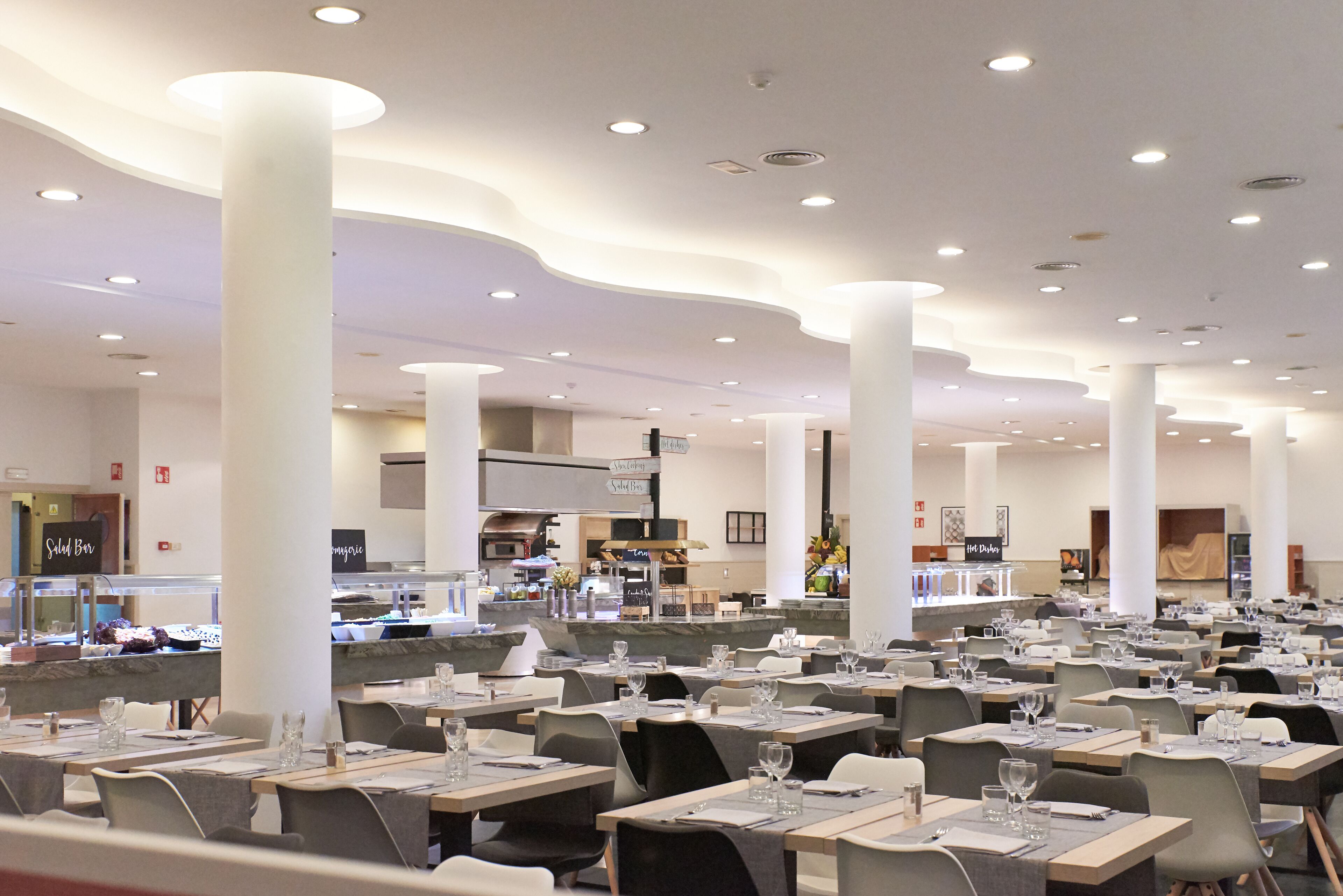 Un amplio comedor con varias mesas y sillas, una zona de cocina central y una mesa de buffet.
