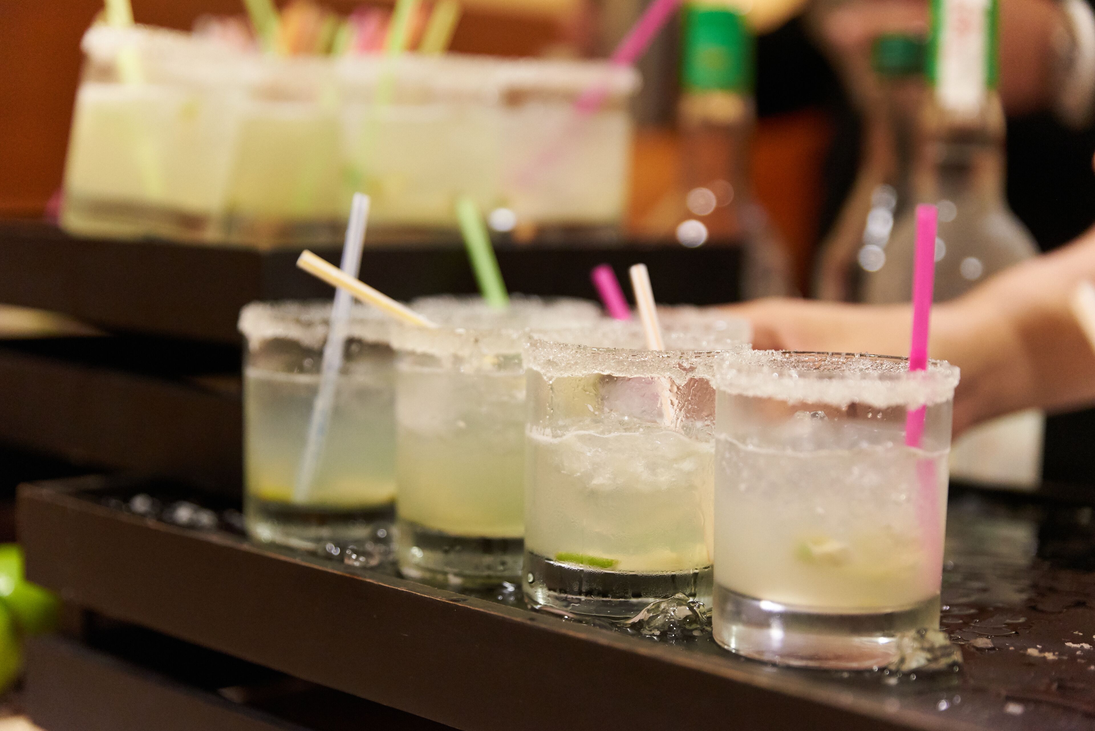 A bar with several glasses of a clear beverage, each with a straw and a lime wedge.