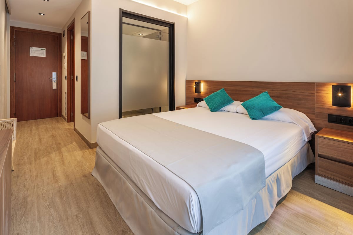 A hotel room with a large bed, a wooden headboard, a nightstand, and a mirror.