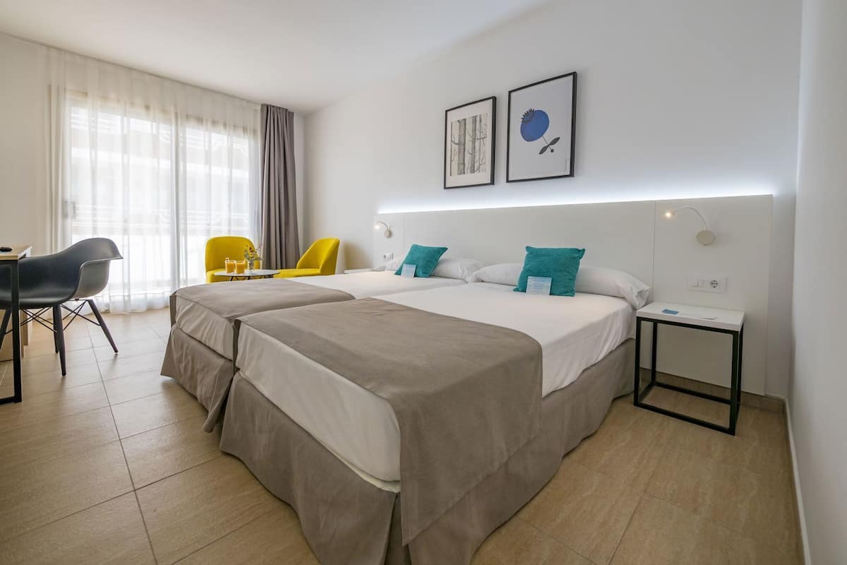A hotel room with two beds, a desk, a chair, and a small table.