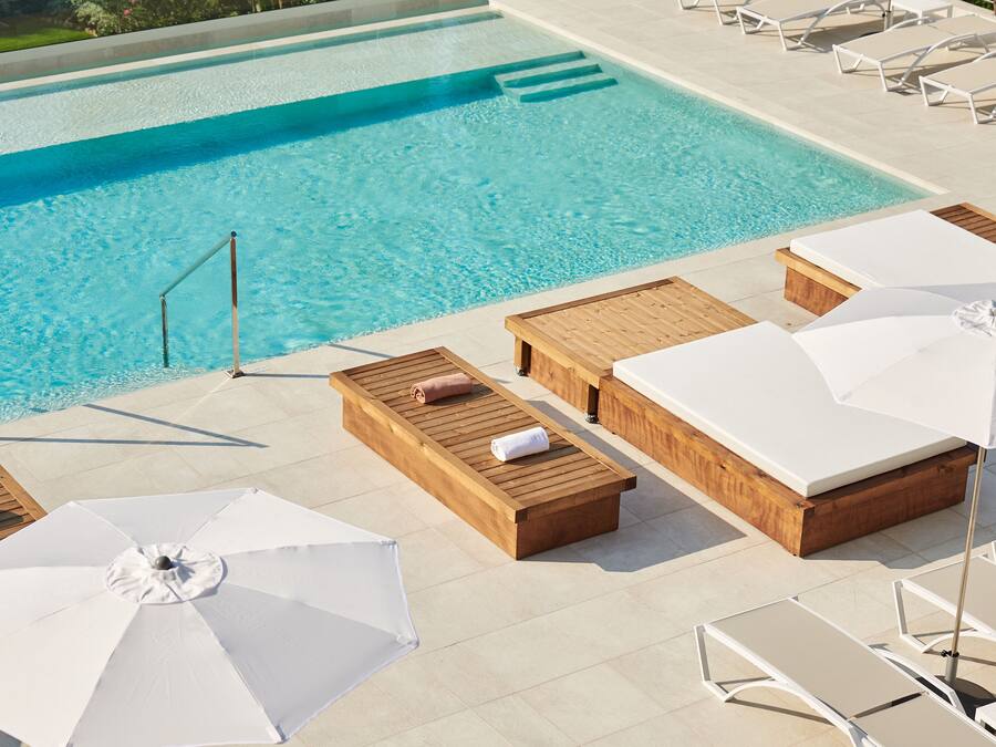A poolside area with lounge chairs, wooden benches, and umbrellas.