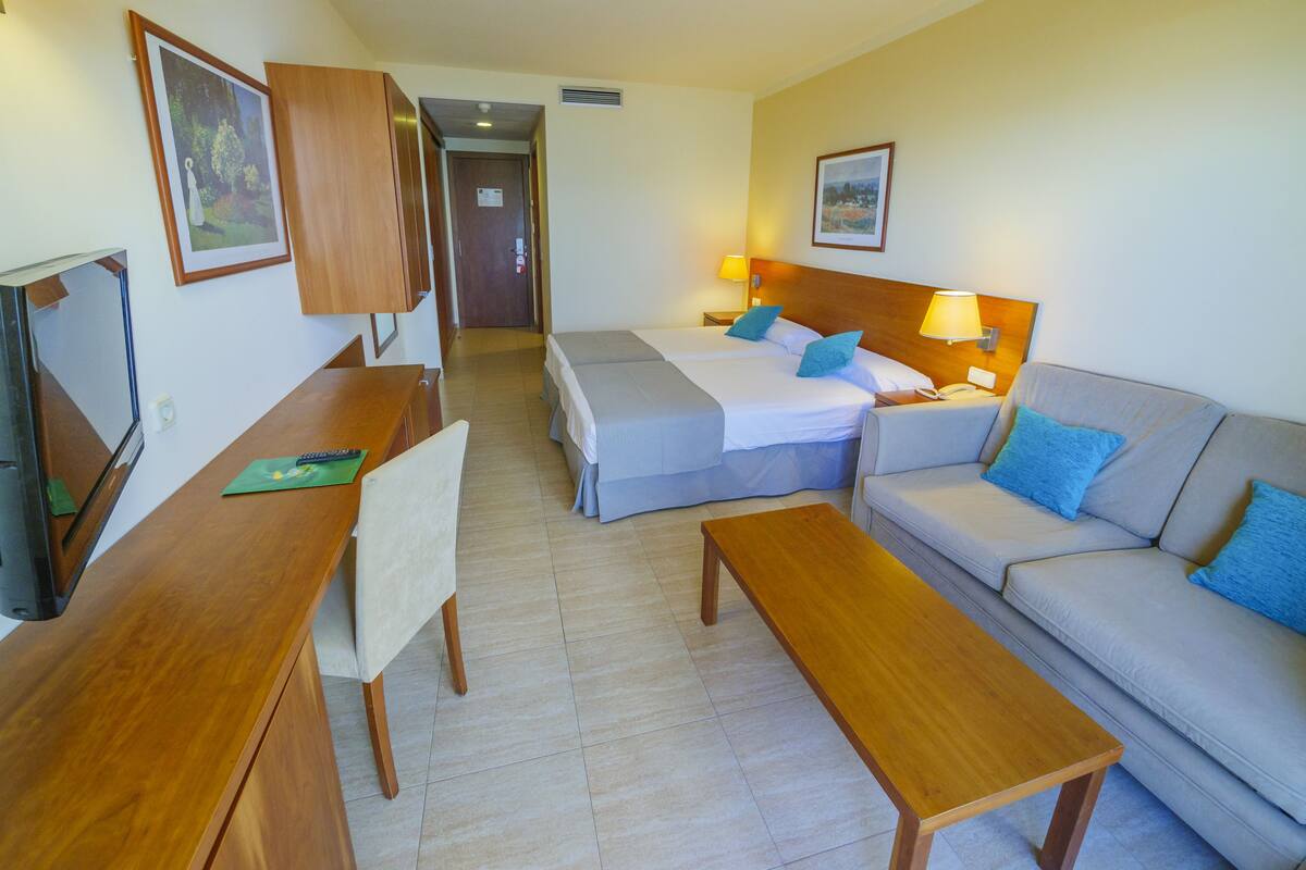 A hotel room with a bed, two bedside tables, a sofa, a desk, and a chair.