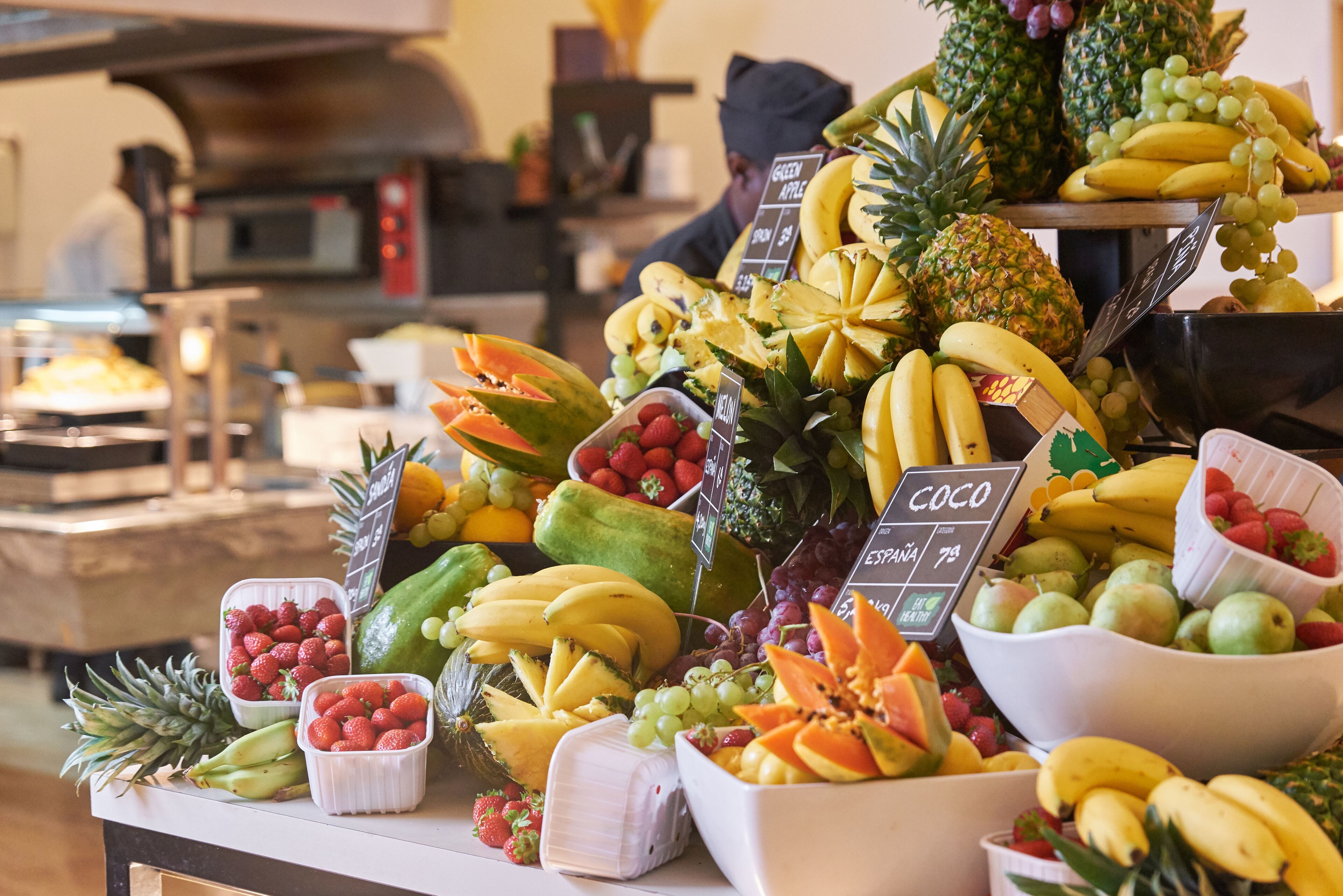 Exhibición de frutas con diversas frutas tropicales y un cartel que indica los precios.