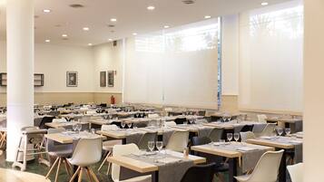 Un salón de conferencias con varias mesas y sillas, una pizarra y una pantalla para proyector.