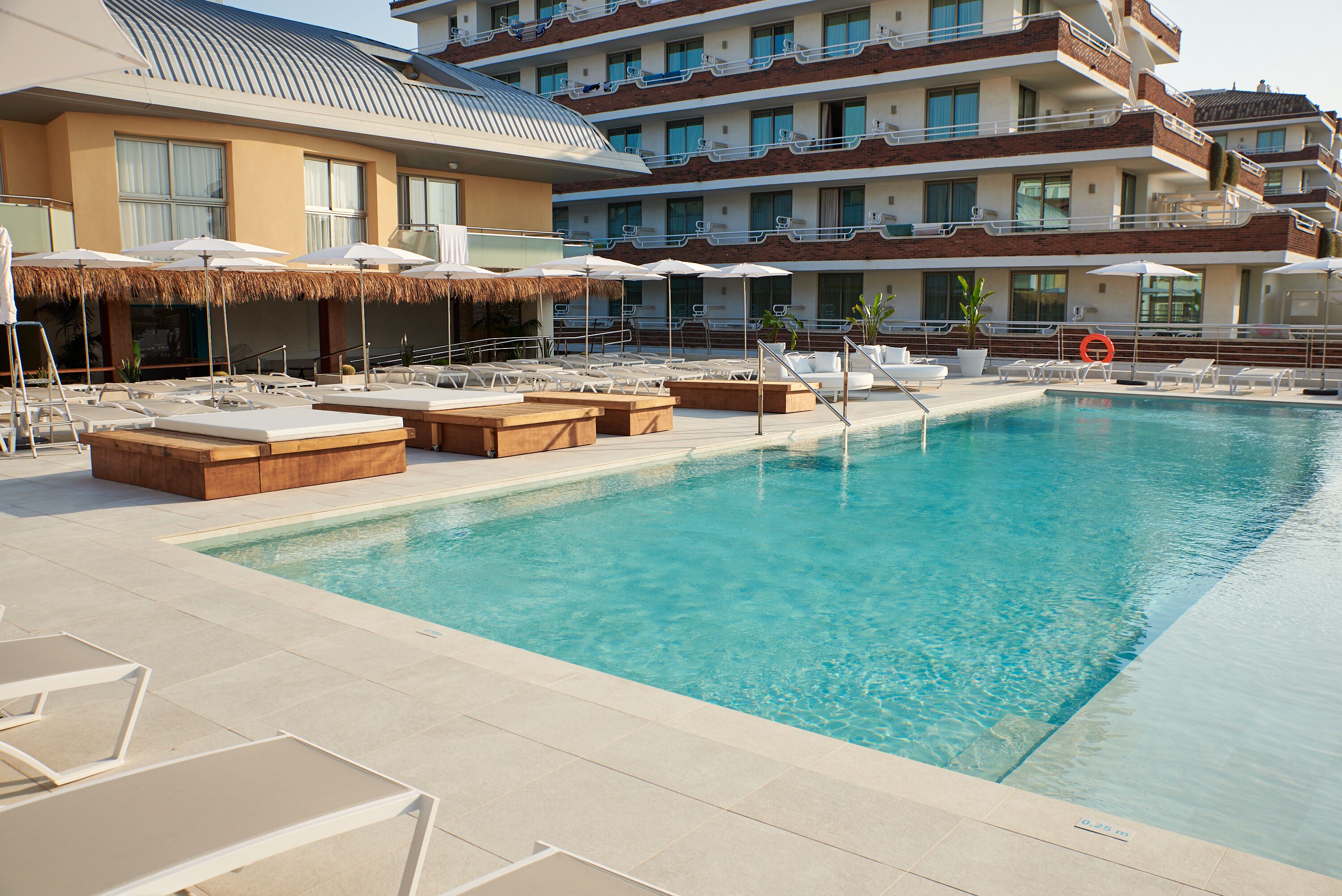 Area piscina di un hotel con sdraio, ombrelloni e una piscina cristallina.