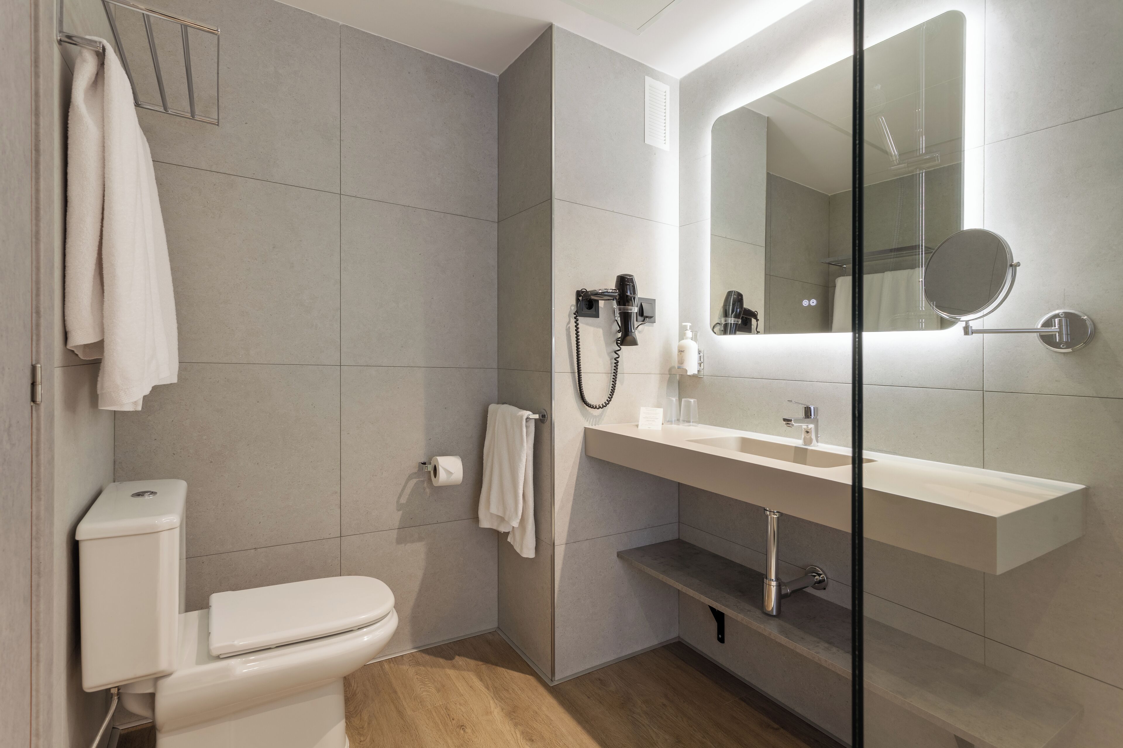 A modern bathroom with a toilet, a sink, a mirror, and a shower area.