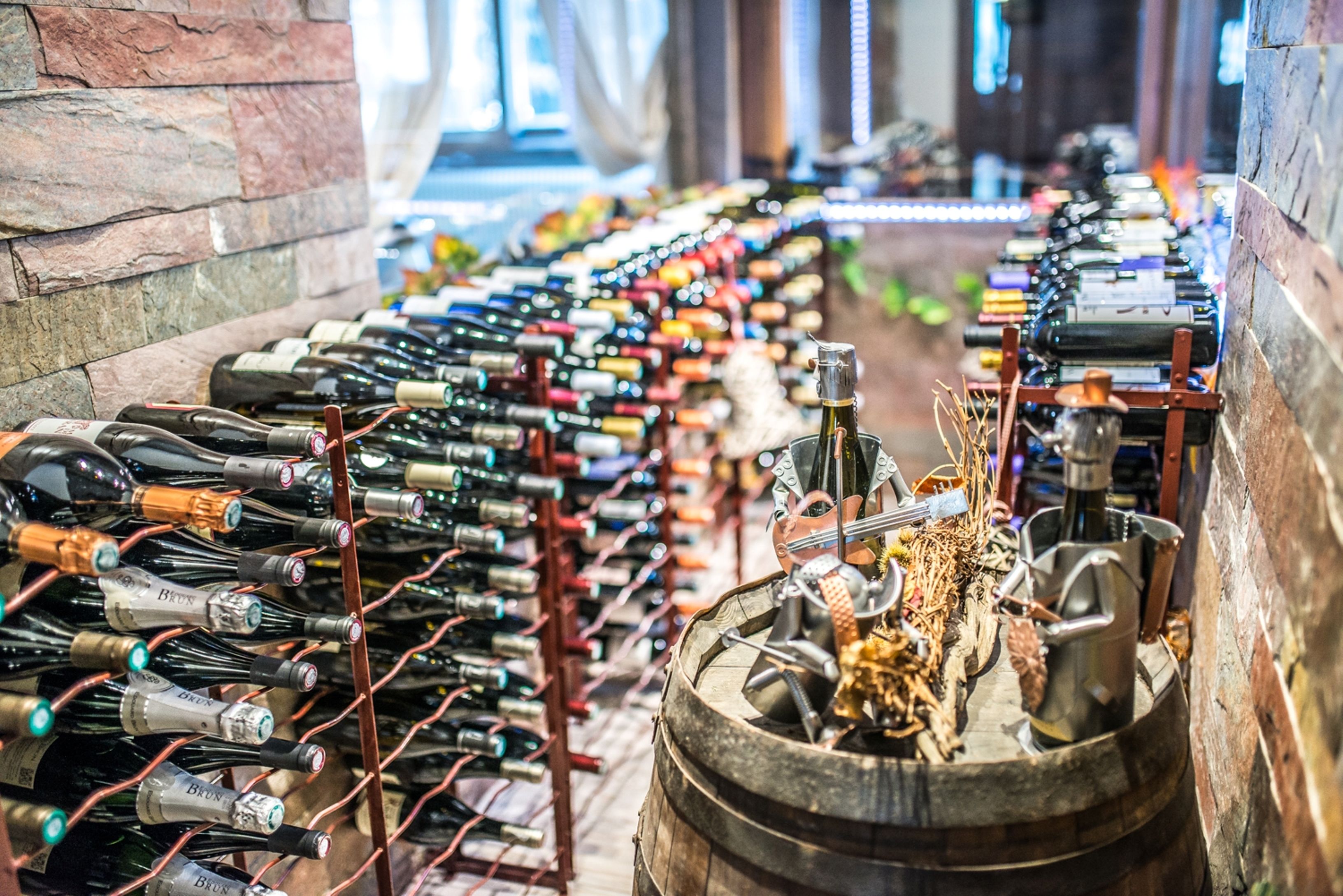 Une cave à vin contenant de nombreuses bouteilles de vin rangées sur des étagères, avec une barrique placée au centre.