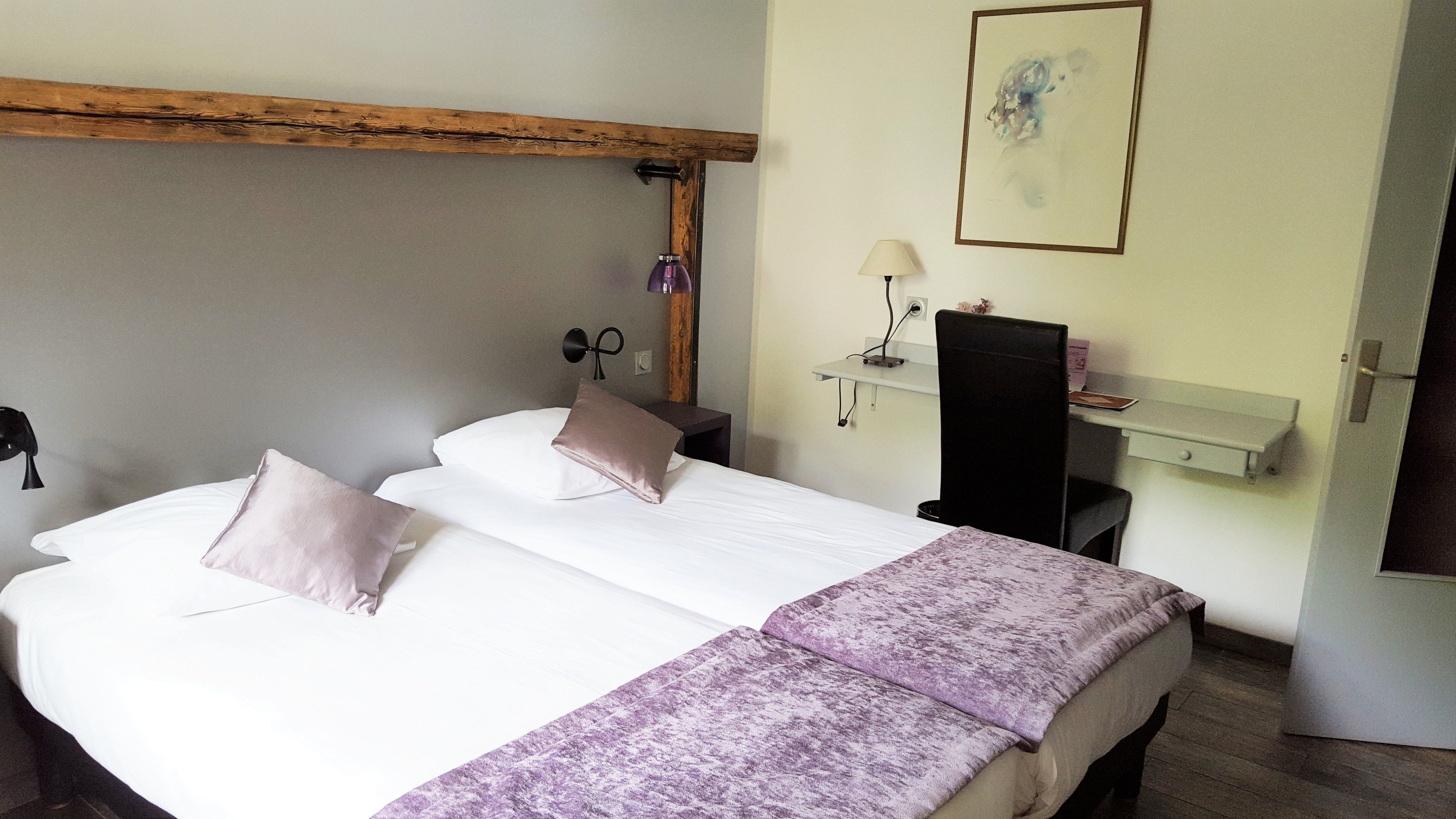 A double bed with two pillows, a bedside table, a lamp, and a small shelf with a book and a box.