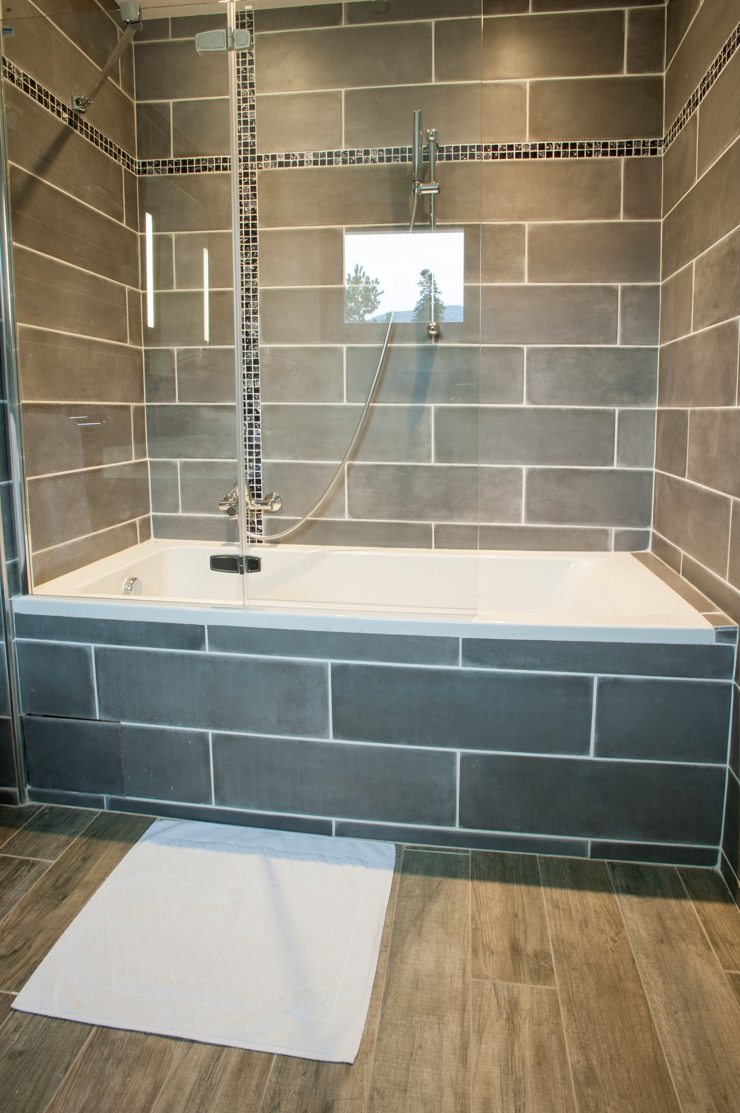 Ein modernes Badezimmer mit einer gläsernen Badewanne, gefliesten Wänden und Holzboden.