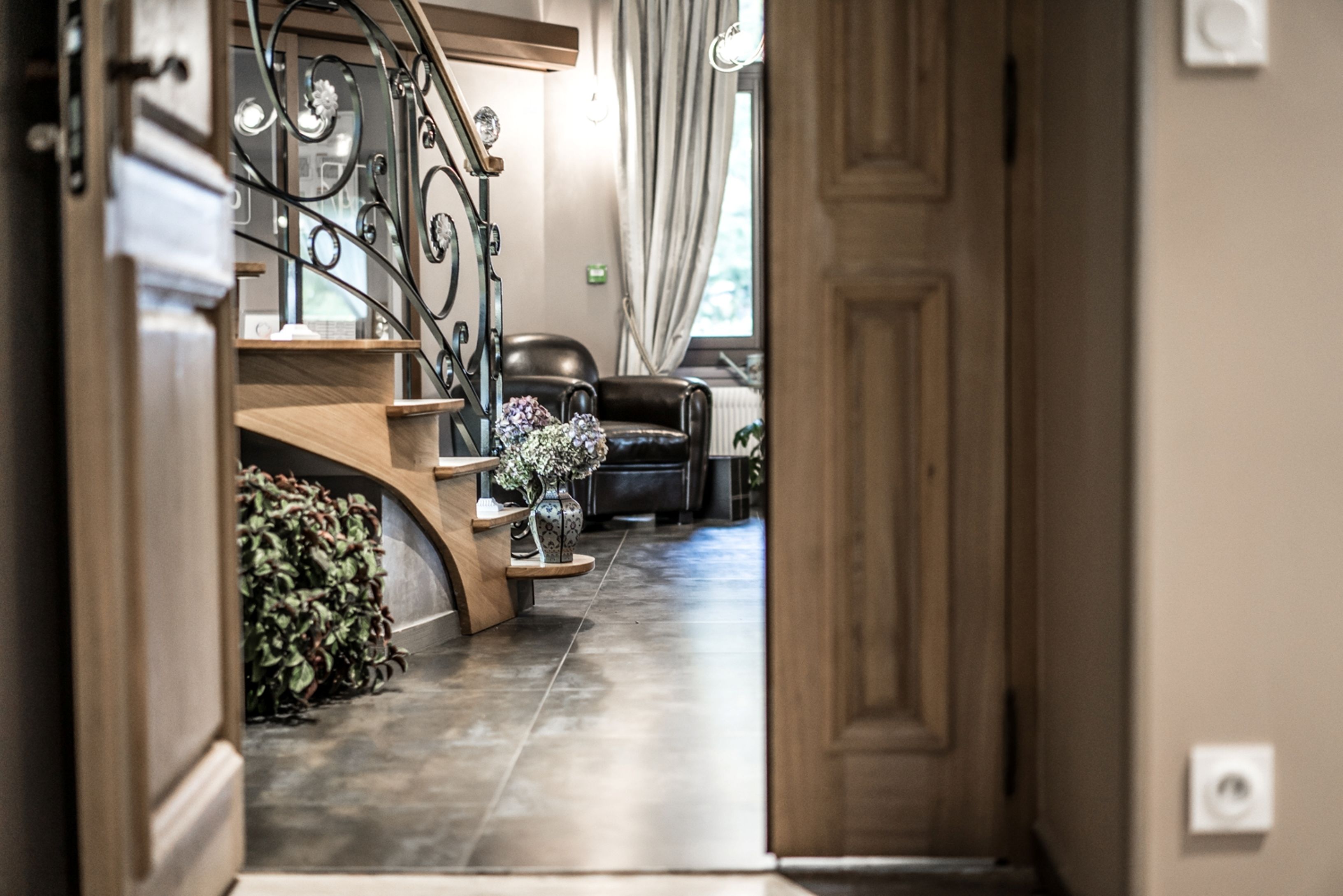 A hallway with a wooden staircase, a leather sofa, and a potted plant.