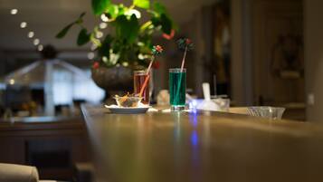 Una zona de bar con dos bebidas sobre la barra, un frutero y una planta en maceta al fondo.