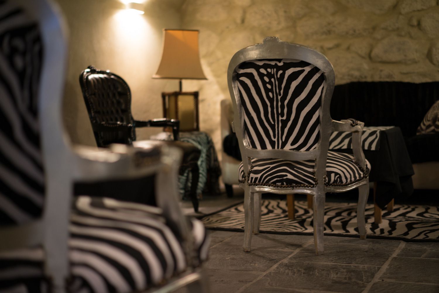 Una habitación con una silla de estampado de cebra, una lámpara y una pared de piedra.