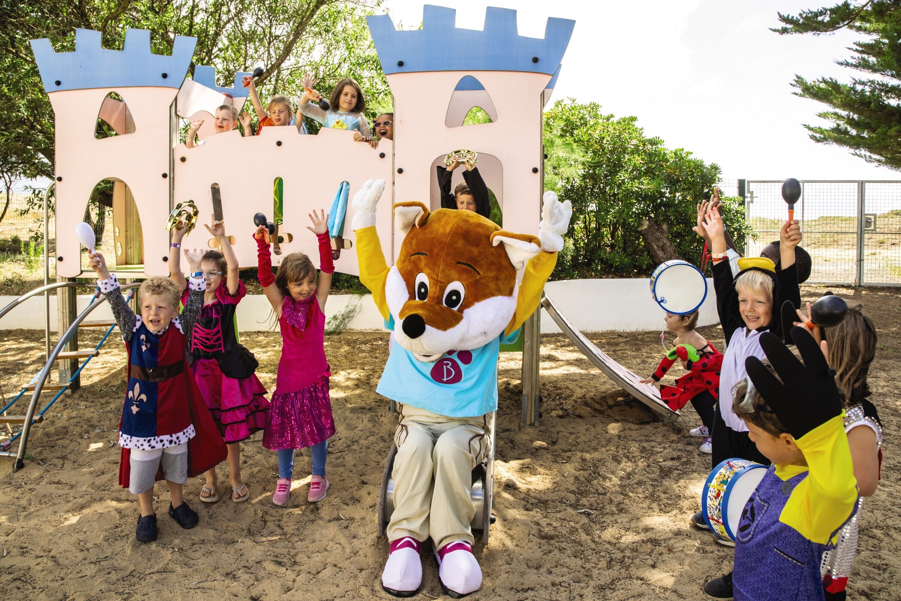 A mascot in a wheelchair interacting with children at a playground with a castle-like structure.