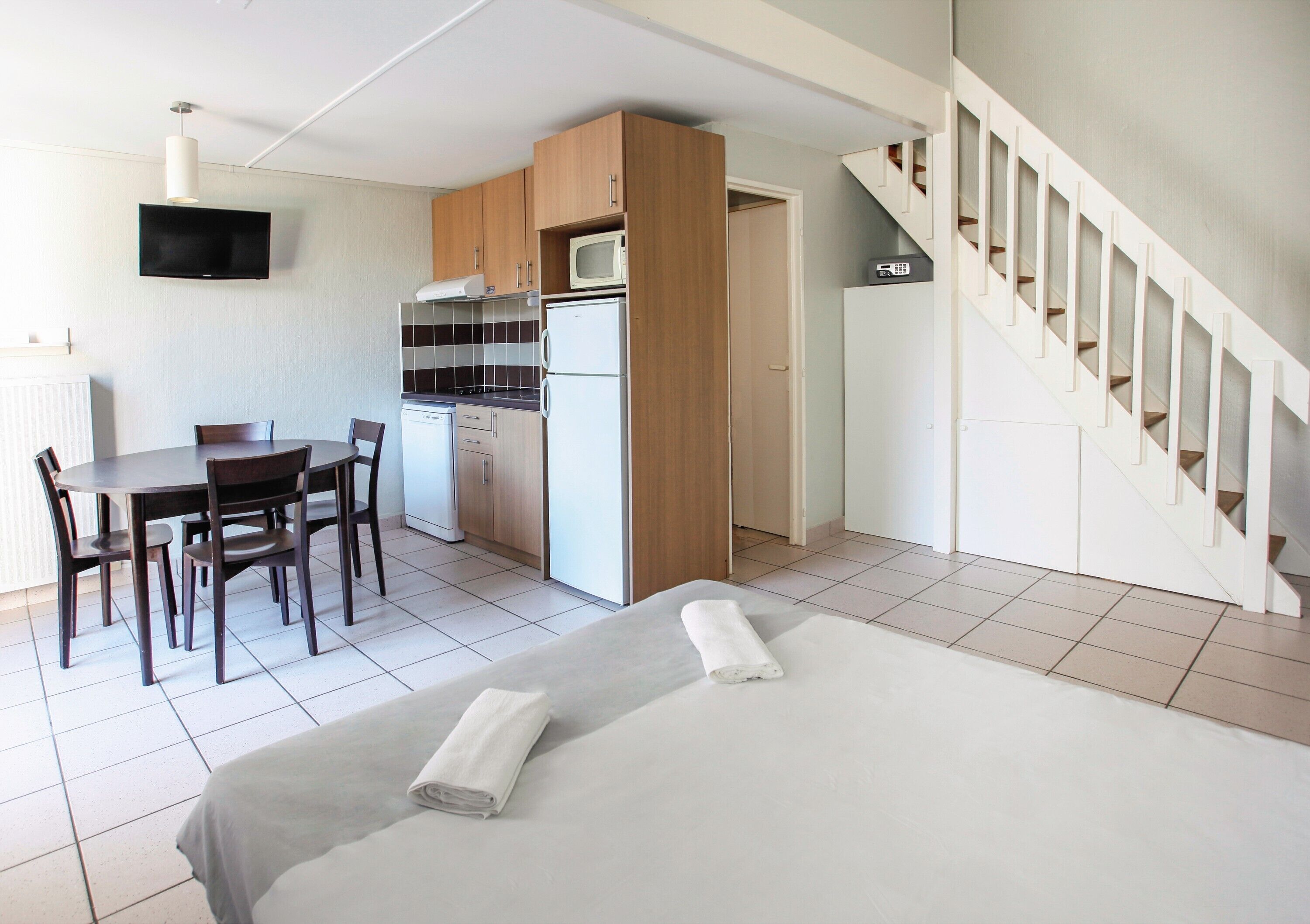 A hotel room with a bed, a desk, a chair, a microwave, a refrigerator, and a staircase.