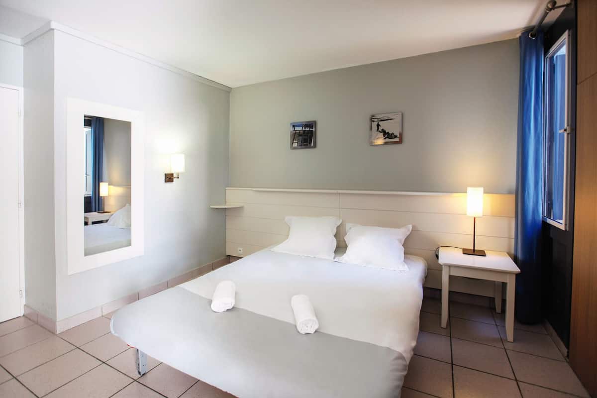 Una habitación de hotel con una cama grande, una mesita de noche, un espejo y una lámpara fijada a la pared.
