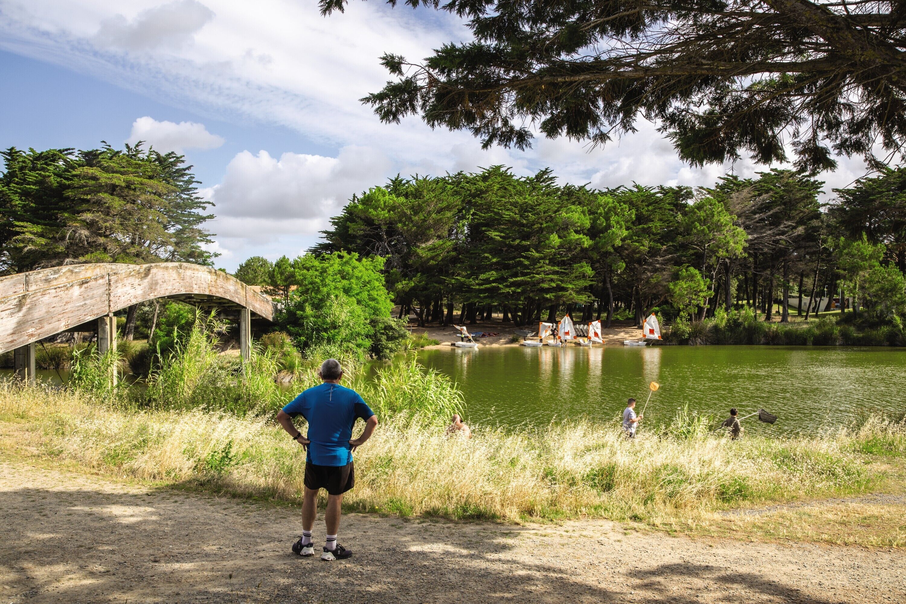 A wooden bridge over a lake with people fishing and a clear sky.