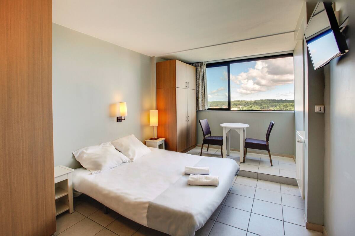 Habitación de hotel con cama, escritorio, silla, televisión y ventana con vistas.