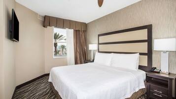 Una camera d'albergo con un letto grande, una ventola a soffitto, una TV, un comodino e una finestra con tende.