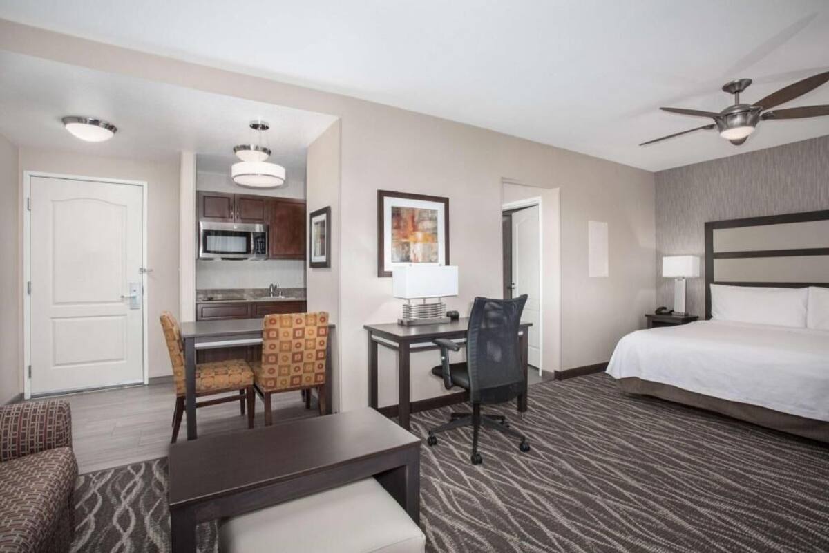 A hotel room with a bed, desk, chair, microwave, and ceiling fan.