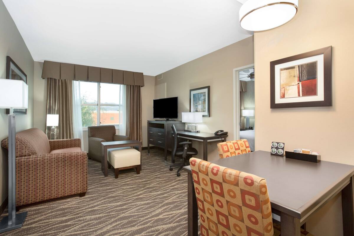A hotel room with a sofa, a desk, a computer, a TV, and a dining table.