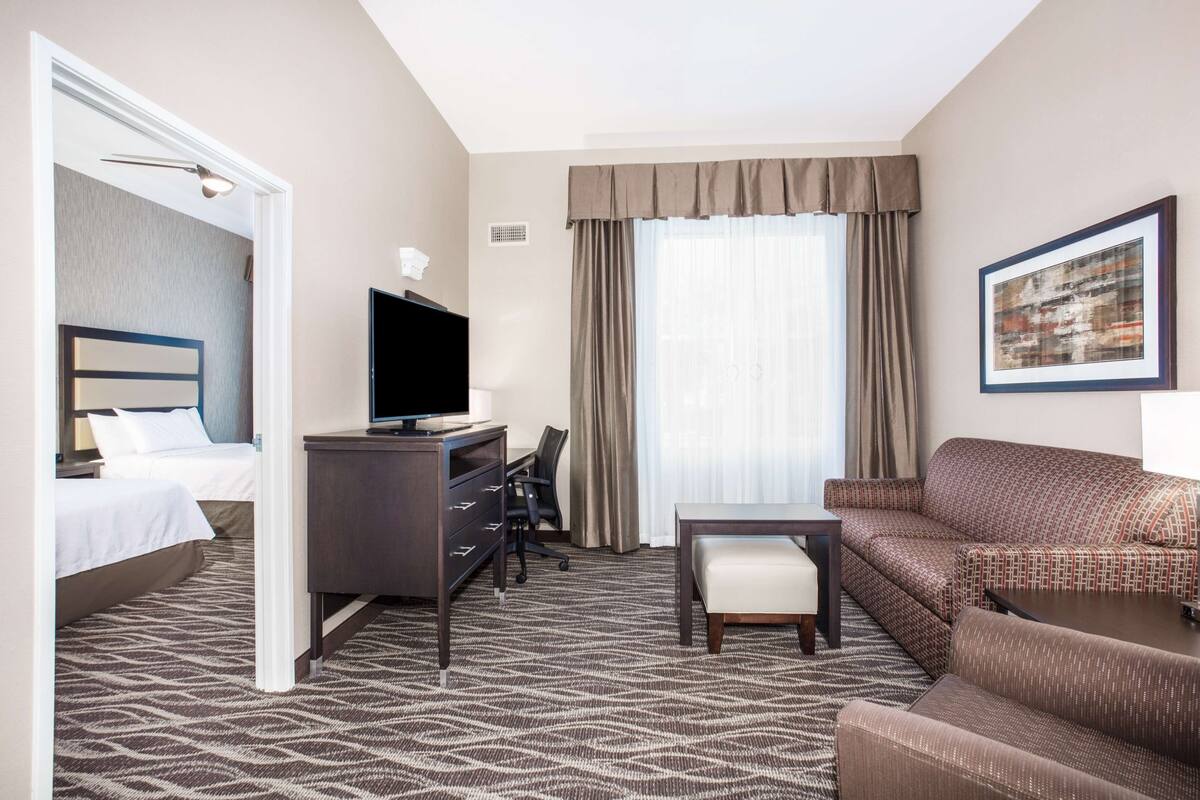 A hotel room with a bed, a desk with a television, a sofa, a chair, and a window with curtains.