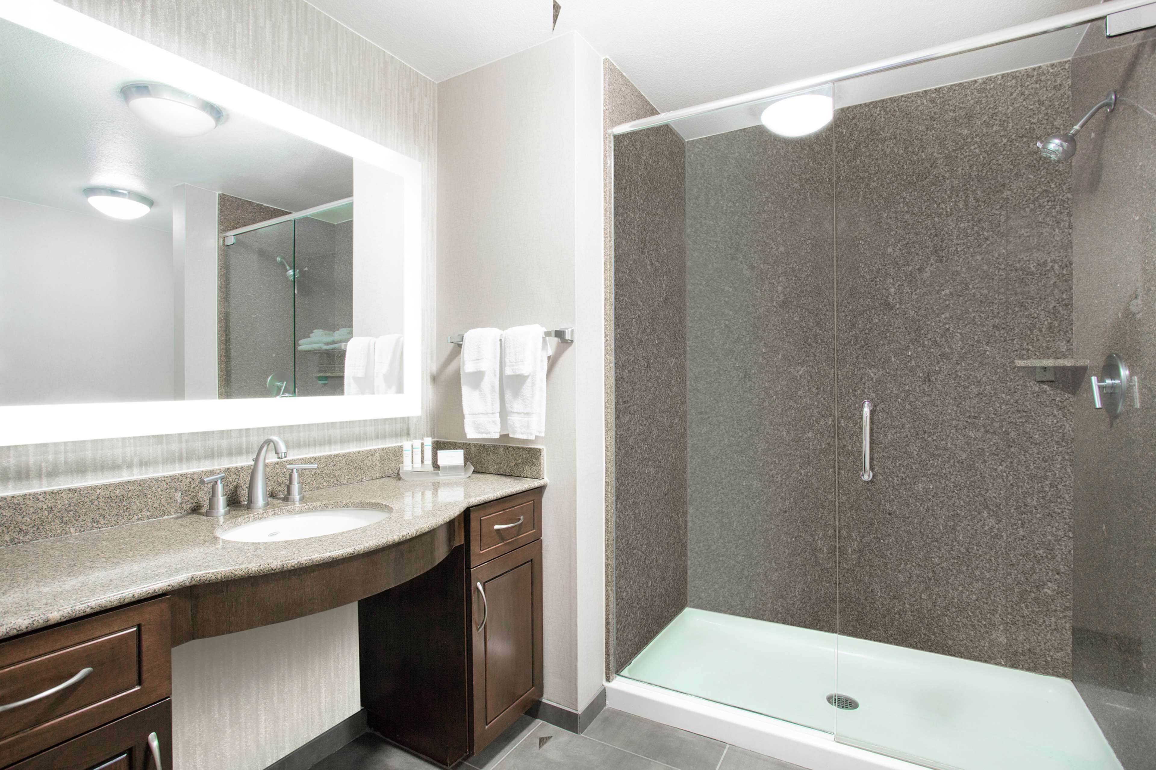 Un baño moderno con un espejo grande, dos lavamanos, una ducha con puerta de cristal y un banco.