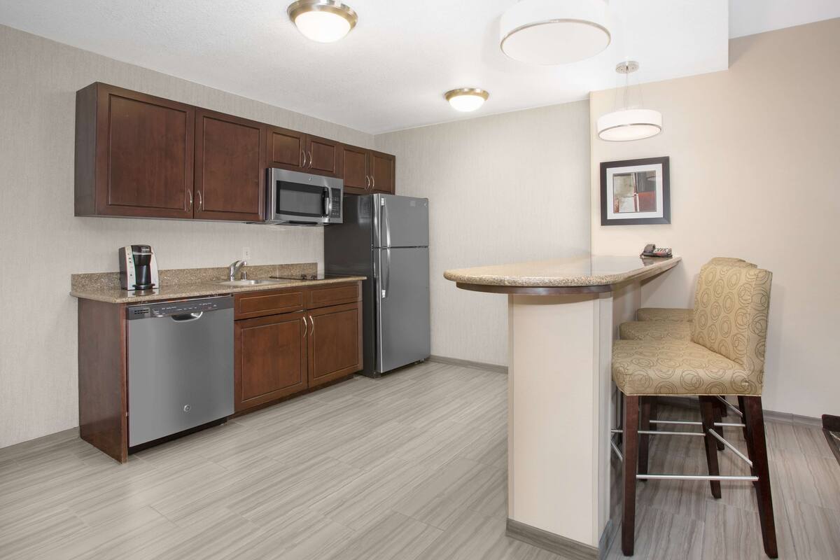 A modern kitchen with wooden cabinets, stainless steel appliances, and a bar stool.